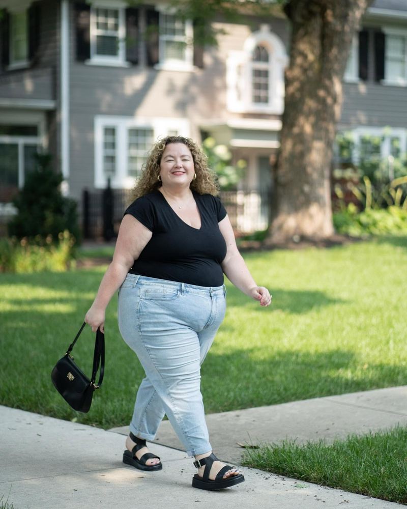 Jessica walking down a tree-lined sidewalk past a gray two-story house